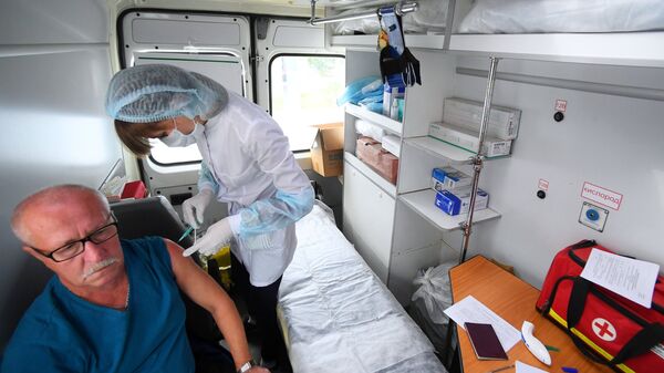 Сотрудник пункта вакцинации делает мужчине прививку против гриппа у станции метро Козья слобода