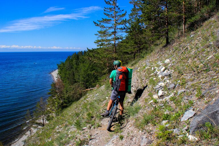 Велосипедист на участке туристического пешего маршрута Большая Байкальская тропа в Прибайкальском национальном парке на берегу озера Байкал