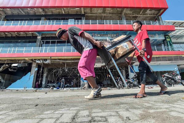 Люди несут товары из торгового центра после землетрясения и цунами в городе Палу, на острове Сулавеси, Индонезия. 30 сентября 2018 года
