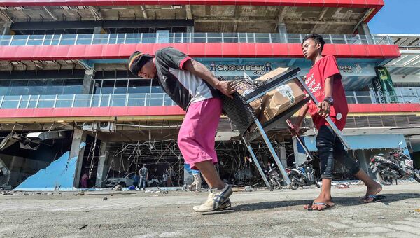 Люди несут товары из торгового центра после землетрясения и цунами в городе Палу, на острове Сулавеси, Индонезия. 30 сентября 2018 года