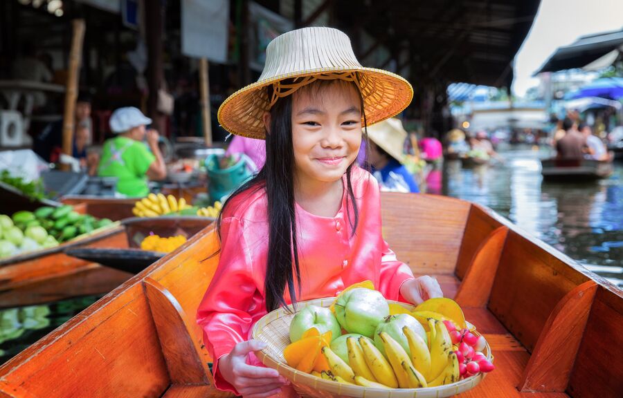 Девочка с корзиной фруктов на плавучем рынке в Таиланде 
