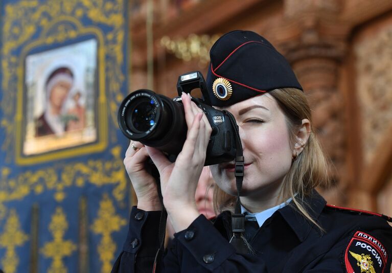 Сотрудник полиции фотографирует во время Божественной литургии в кафедральном соборе Успения Пресвятой Богородицы в Астрахане