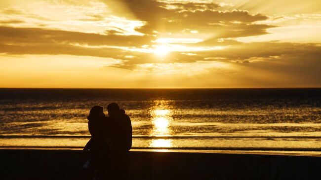 Молодые люди встречают закат на пляже