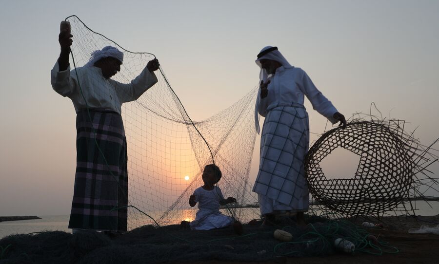 Мужчины обучают ребенка ремеслам во время фестиваля парусного спорта  у побережья Далмы, ОАЭ 