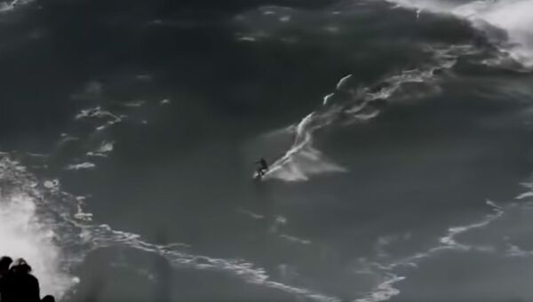Кадр из видео, на котором серфер бопадает под огромную волну в Португалии
