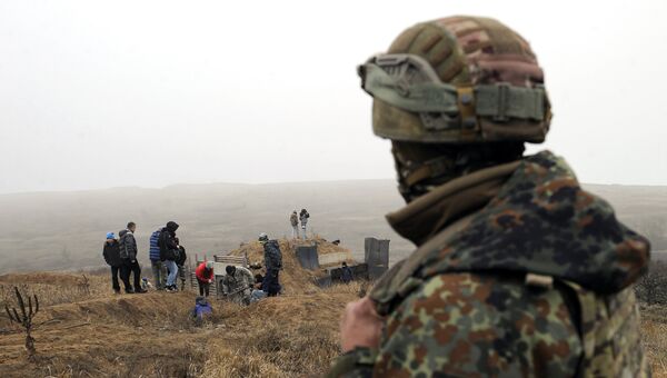 Украинский военнослужащий смотрит на активистов, копающих траншеи на побережье Азовского моря у города Мариуполь. 26 ноября 2018