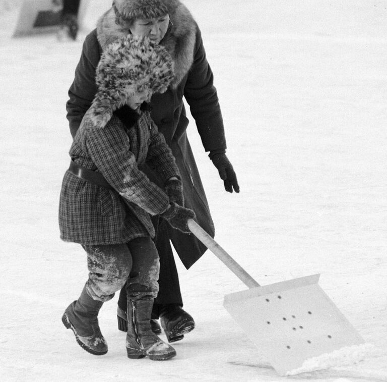 Ребенок убирает лопатой снег на катке