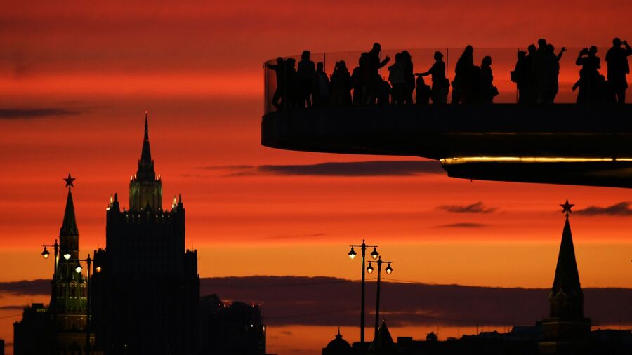 Посетители на Парящем мосту в природно-ландшафтном парке «Зарядье» в Москве. На дальнем плане: Московский Кремль и высотное здание Министерства иностранных дел России