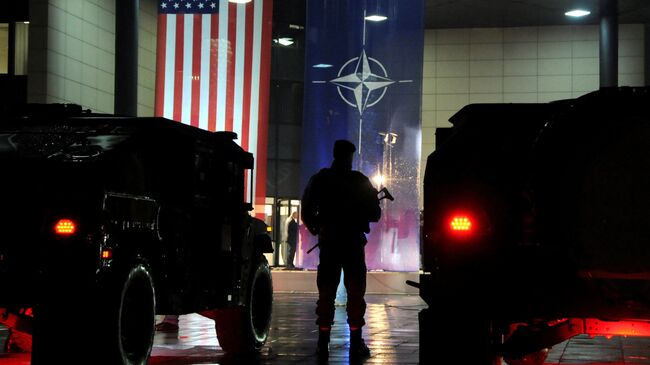 Военнослужащий сил безопасности Косово стоит перед флагами США и НАТО в Приштине