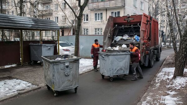 Сотрудники коммунальных служб выгружают мусор из контейнеров в мусоровоз