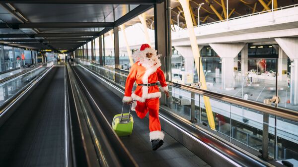 Мужчина в костюме Деда Мороза бежит с чемоданом в аэропорту 