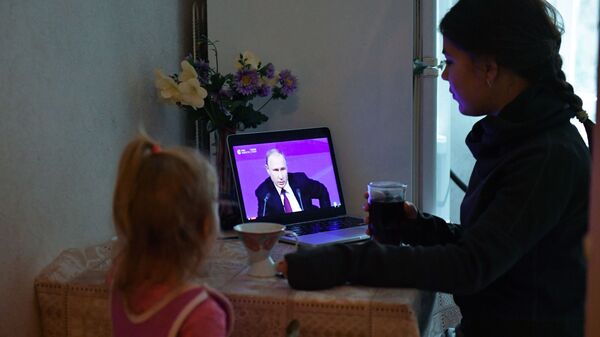 Женщина с ребенком в Симферополе смотрит прямую трансляцию ежегодной большой пресс-конференции президента РФ Владимира Путина
