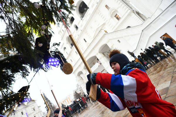 Ученик школы олимпийского резерва по хоккею украшает игрушечной клюшкой новогоднюю елку на Соборной площади Московского Кремля