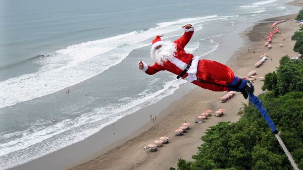 Банджи-джампер, одетый как Санта-Клаус, прыгает с платформы над пляжем в Куте, Бали