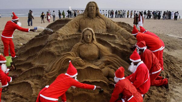 Художники в костюмах Санта Клауса создают песчаную скульптуру в канун Рождества на пляже города Пури, Индия