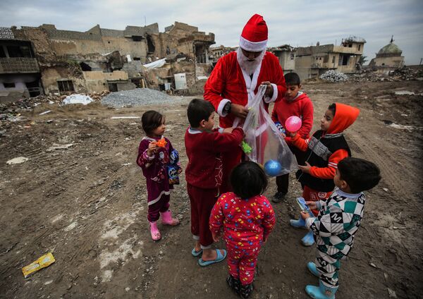 Мужчина, переодетый в Деда Мороза, раздает детям подарки на одной из улиц Мосула, Ирак 