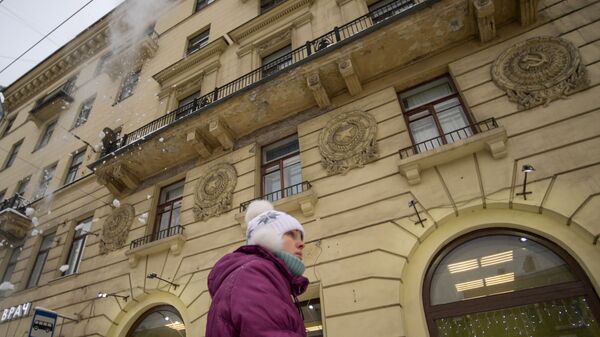 Женщина идет по Суворовскому проспекту в Санкт-Петербурге, где работники коммунальных служб убирают снег с крыш домов