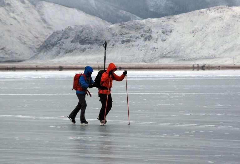 Туристы катаются на коньках по льду замерзшего озера Байкал