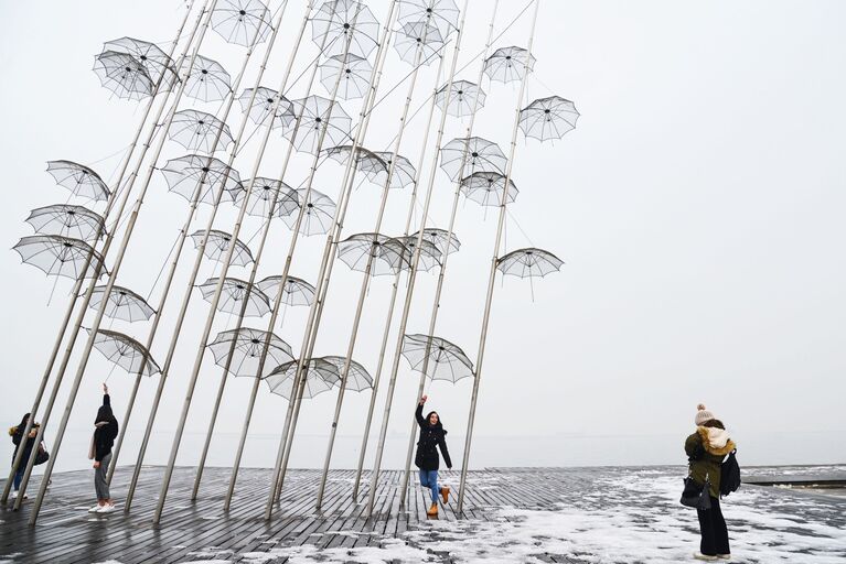 Девушки фотографируются на фоне инсталляции Зонтики на набережной в Салониках