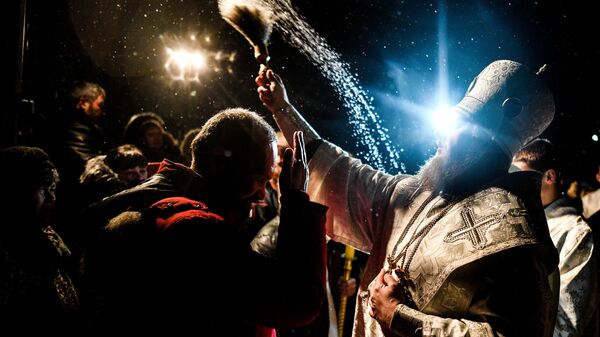 Священник окропляет святой водой присутствующих во время традиционных купаний в праздник Крещения у церкви Сорока Мучеников Севастийских в Переславле-Залесском. 19 января 2019