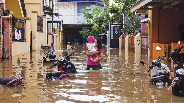 Женщина несет свою дочь во время наводнения в Макассаре, Индонезия