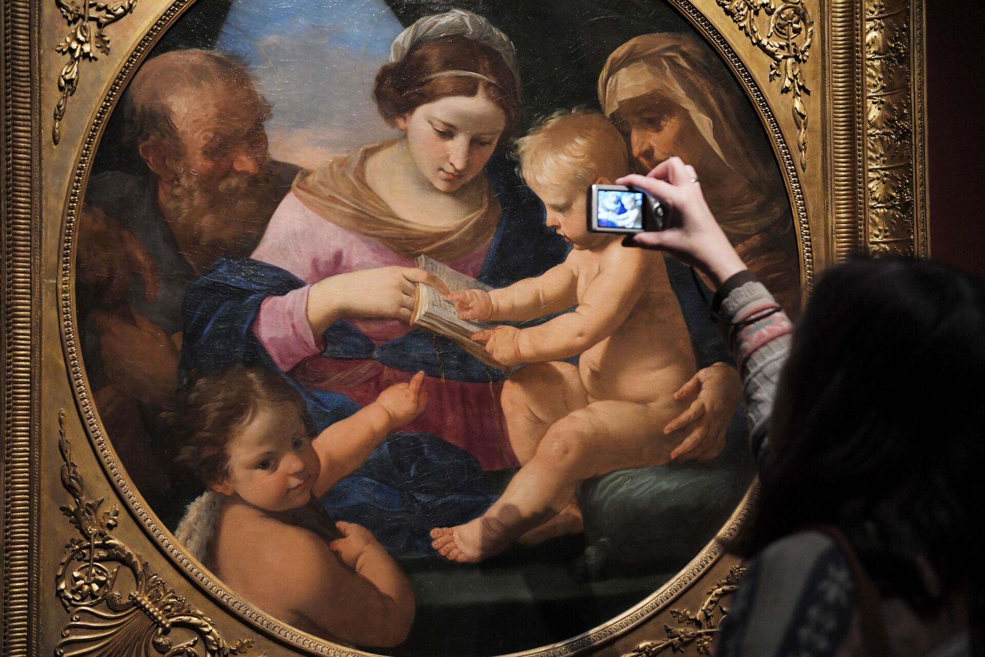 Посетительница фотографирует картину Святое семейство с маленьким Иоанном Крестителем и Святой Елизаветой Симоне Кантарини на выставке Гости из Неаполя. Артемизия Джентилески и современники - РИА Новости, 1920, 31.10.2025