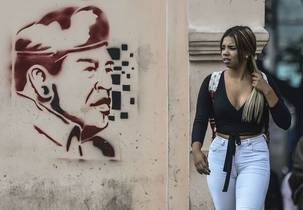 Девушка проходит мимо граффити бывшего президента Венесуэлы Уго Чавеса в Каракасе