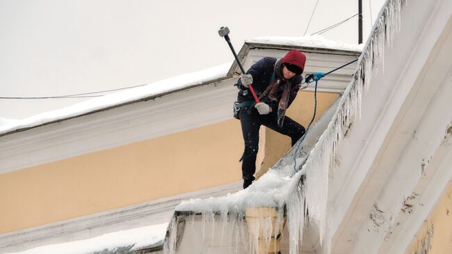 Работник коммунальной службы чистит от снега и сосулек крышу дома в Санкт-Петербурге