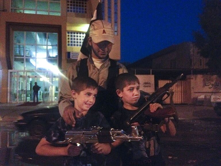 Боец ИГ (деятельность запрещена в РФ) фотографируется с детьми, держащими оружие, в Мосуле, Ирак. 2014 год Боец ИГ (деятельность запрещена в РФ) фотографируется с детьми, держащими оружие, в Мосуле, Ирак. 2014 год