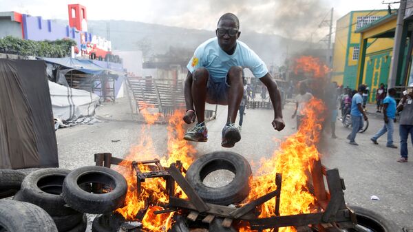 Протестующий перепрыгивает через горящую баррикаду во время акции протеста против правительства на улицах Порт-о-Пренса, Гаити