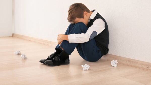 Расстроенный ребенок сидит на полу в школе 