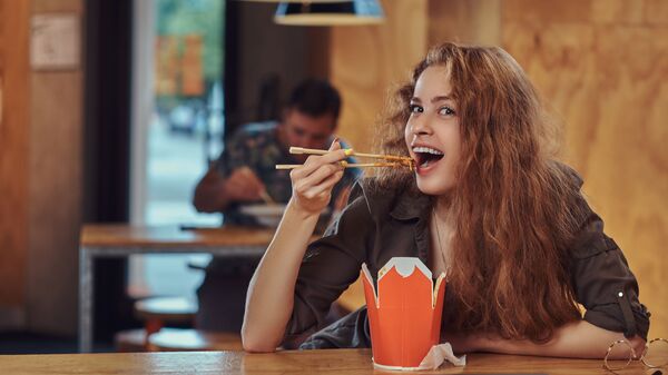 Девушка ест лапшу в кафе