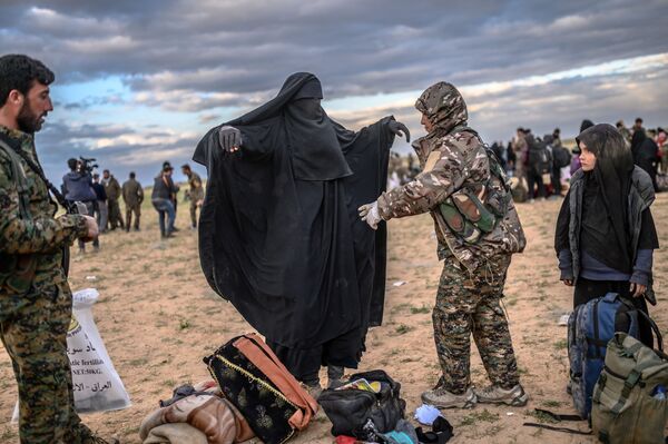 Боец Сирийских демократических сил (СДС) проверяют женщину в деревне Багуз провинции Дейр-эз-Зор
