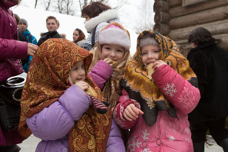 Дети едят блины во время праздничных гуляний на Масленицу