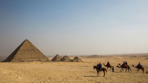Группа туристов верхом на лошадях и верблюдах во время экскурсии к древнеегипетским пирамидам в Эль-Гизе, пригороде Каира
