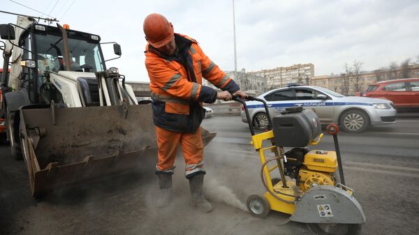 Рабочий бригады ГБУ Автомобильные дороги проводит латочный ремонт дорожного покрытия в Москве