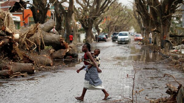 Женщина с ребенком на спине пересекает улицу после циклона Идаи в Бейре, Мозамбик