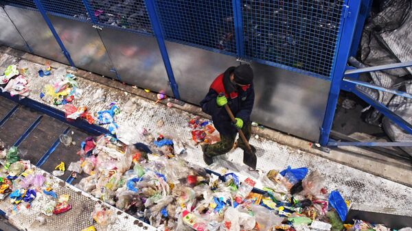 Работник поправляет мусор на конвейере завода по переработке отходов