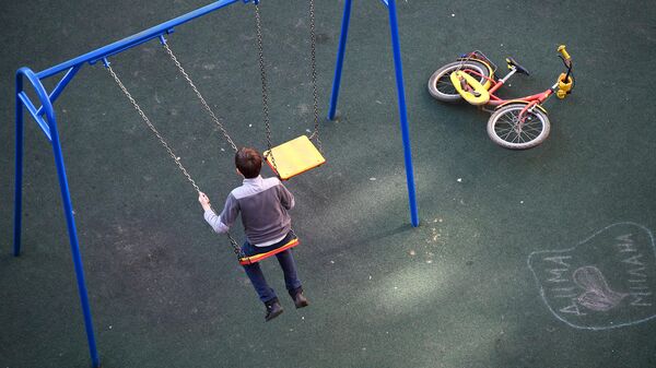Мальчик качается на качелях на детской площадке