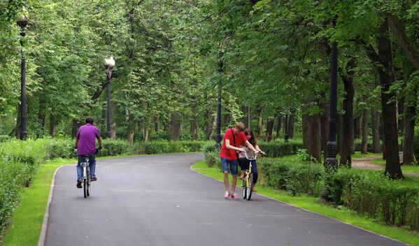 Юноша учит девушку ездить на велосипеде на одной из аллей Измайловского парка в Москве