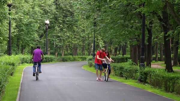 Юноша учит девушку ездить на велосипеде на одной из аллей Измайловского парка в Москве