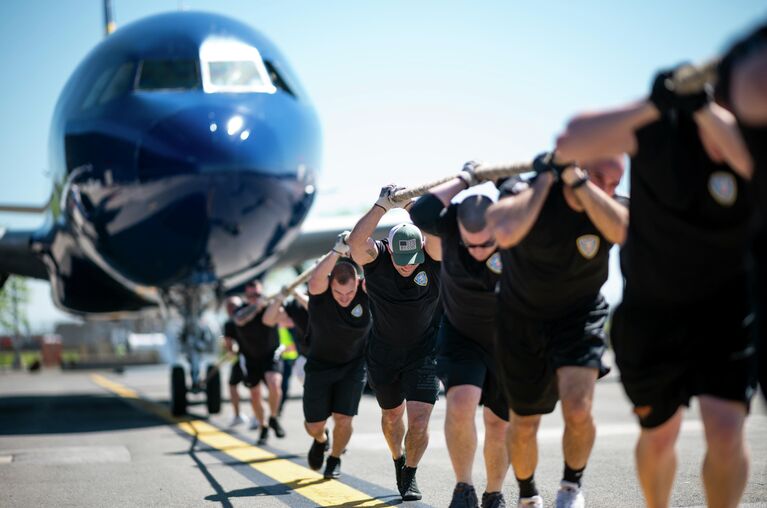 Мужчины тянут самолет JetBlue A320 во время ежегодных соревнований Plane Pull в Международном аэропорту Джона Ф. Кеннеди