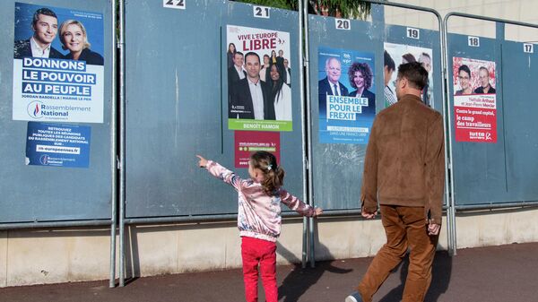Избиратели у предвыборных плакатов кандидатов в заключительный день голосования на выборах в Европейский парламент у избирательного участка в Париже