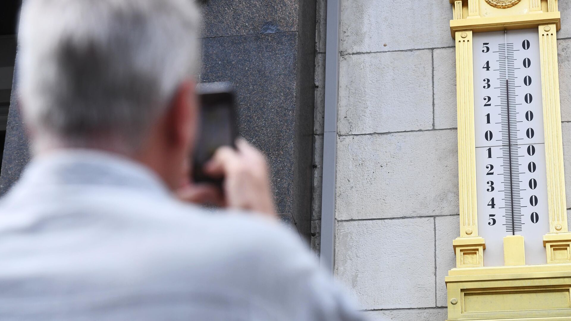 Мужчина фотографирует термометр на здании Государственной Думы РФ в Москве - РИА Новости, 1920, 24.05.2023