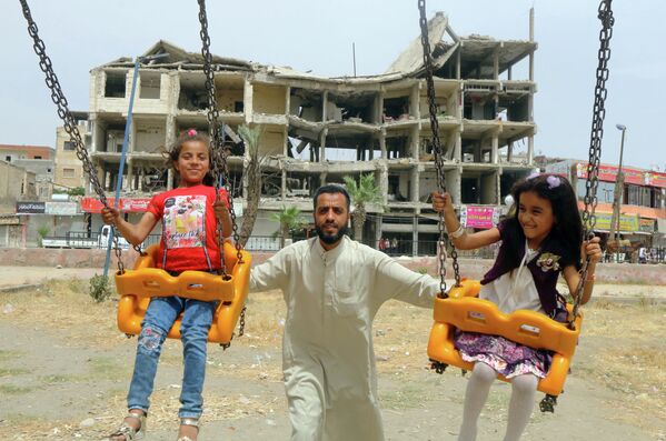 Девочки катаются на качелях возле поврежденного здания в первый день мусульманского праздника Ид аль-Фитр в городе Ракка, Сирия