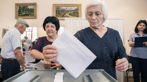 Женщина опускает бюллетень в урну для голосования на выборах в Южной Осетии