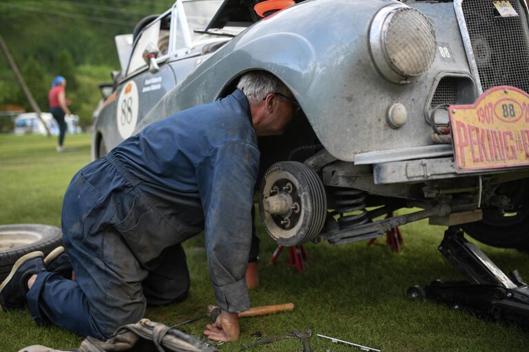 Участник международного ралли на старинных автомобилях Пекин - Париж 2019 на месте ночной стоянки возле села Чибит в Республике Алтай ремонтирует свой автомобиль Sunbeam Alpine (1954 г.)