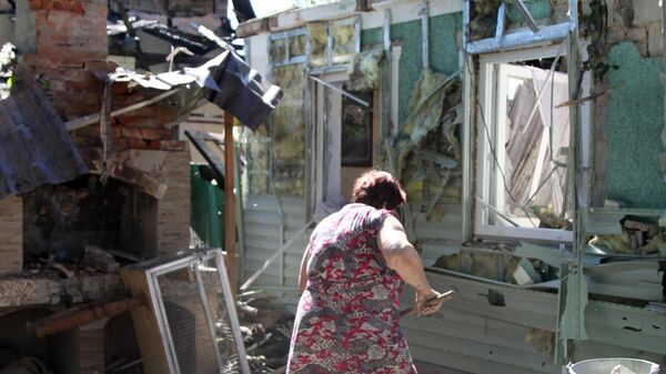 Женщина убирает мусор во дворе жилого дома в Донецке, пострадавшего в результате обстрела