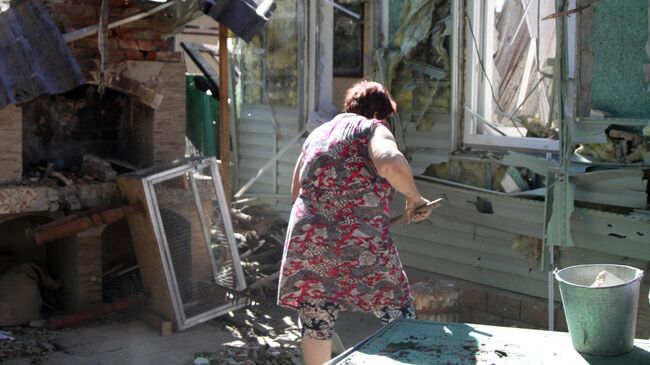 Женщина убирает мусор во дворе жилого дома в Донецке, пострадавшего в результате обстрела