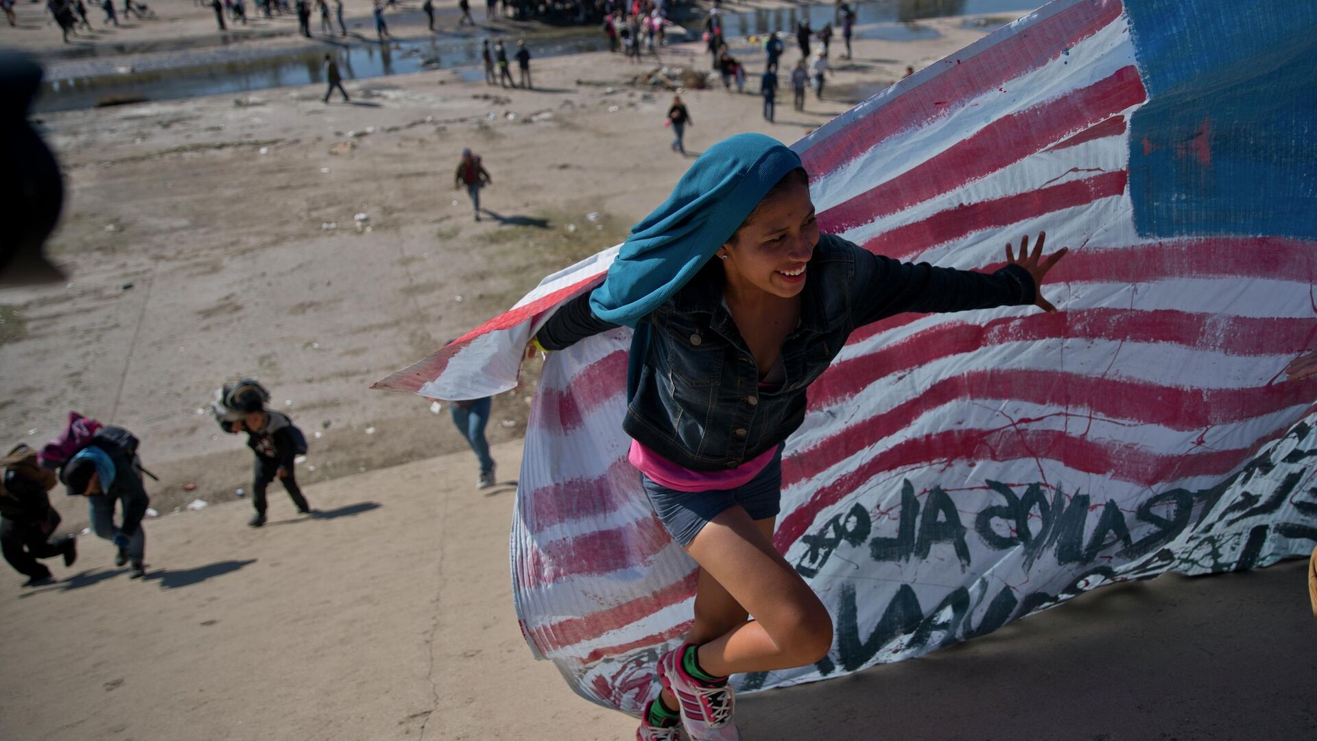 Мигрантка помогает нести американский флаг на границе Мексики и США - РИА Новости, 1920, 20.03.2024